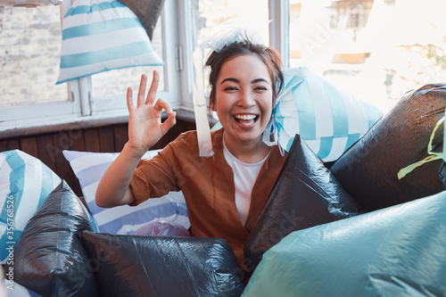 Laughing female surrounded by garbage bags showing okay gesture at camera