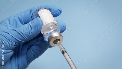 Hand holding glass vial with medical drug being aspirated to a syringe as a treatment or vaccine