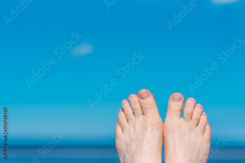 woman legs with beige pedicure on a blue sea background. The image in the lower right corner of the frame.