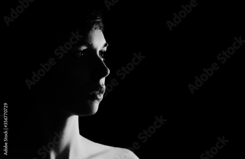 Black and white backlit portrait of young woman on black background