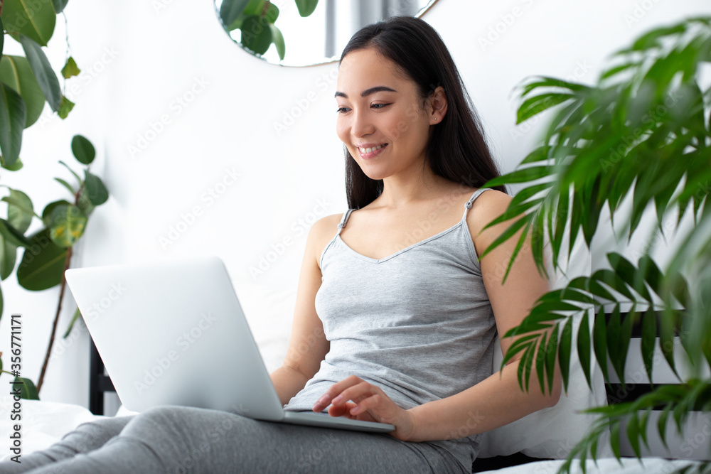 Smiling pretty lady relaxing with laptop in bedroom Smiling pretty lady relaxing with laptop in bedroom