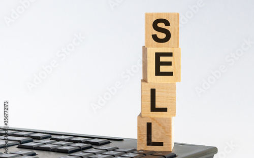 Wooden cubes with word SELL on white background, black keyboard background. Cubes with black letters. photo