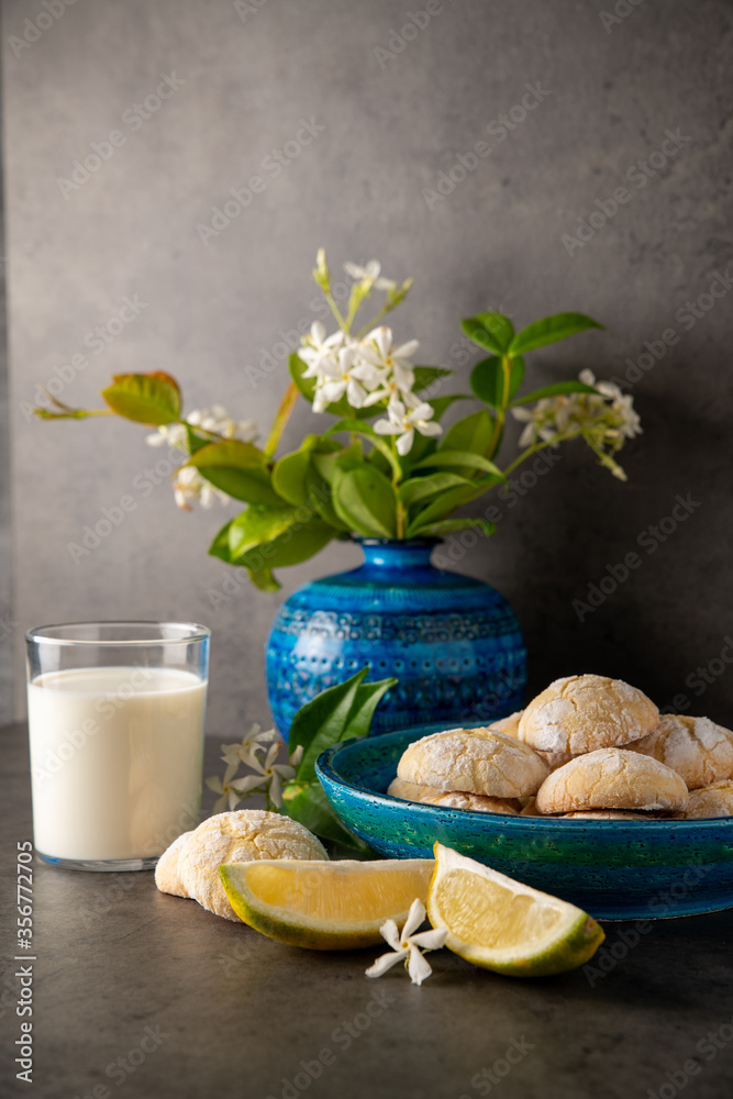 still life on a dark background. lemon cookies and a slice of lemon on the table, a glass of milk and flowers in a vase, vertical position