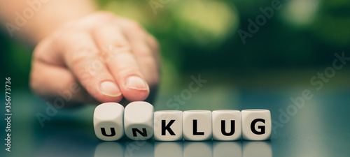 Fotografie Hand dreht Würfel und ändert das Wort unklug in klug.
