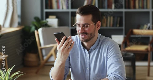 Happy handsome businessman dictating audio message on smartphone in social network application. Smiling young man activating voice assistant, having mobile conversation or search information online. photo