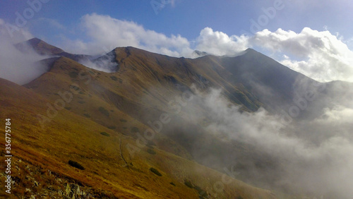 Mountain ridge with a mountain trail with white clouds on a sunny autumn day without people