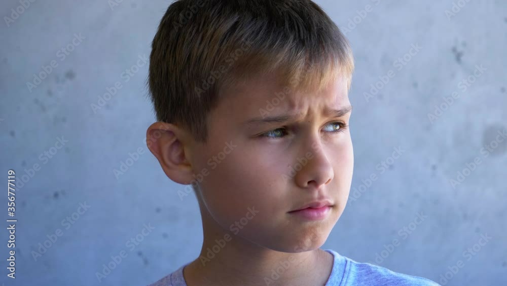 Portrait teen boy raises his lowered head and looks to the side. Kid standing near grungy gray wall Portrait teen boy raises his lowered head and looks to the side. Kid standing near grungy gray wall