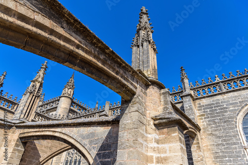 Roof of Seville Cathedral - Close-up low-angle view of the pinnacles and flying buttresses on the roof of Seville Cathedral, under bright sunlight and against clear blue sky. Seville, Andalusia, Spain photo