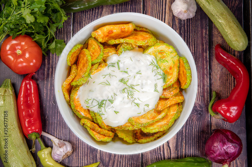 Delicious fried zucchini with, dill and yogurt sauce in a bowl on a wooden table, top view