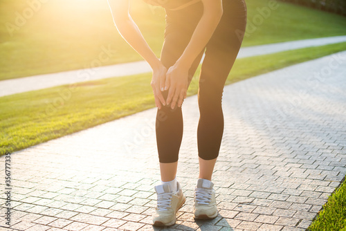 young woman goes in for sports in the park and suffers from knee pain. summer, sun, sun glare, but pain overshadows leisure. sports, pain, treatment.