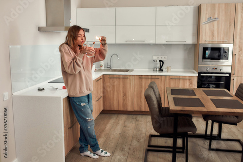 Give relax to your body. Full-length shot of young caucasian woman lighting cannabis in the bowl of glass water pipe or bong while standing in the kitchen. Cannabis and weed legalization concept