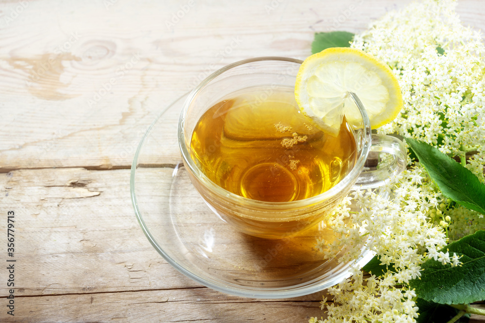 Elderflower tea with lemon and some blossoms on a rustic wooden table, natural home remedy for blood cleansing and against cold and fever, copy space Elderflower tea with lemon and some blossoms on a rustic wooden table, natural home remedy for blood cleansing and against cold and fever, copy space