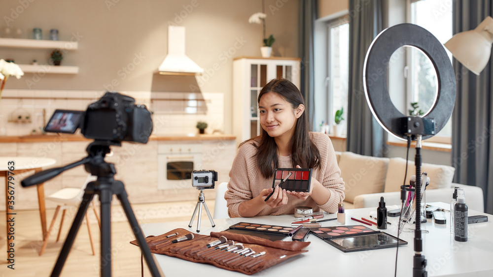 This is the future. Asian female blogger showing cosmetic products while recording a tutorial video for her beauty blog using camera at home