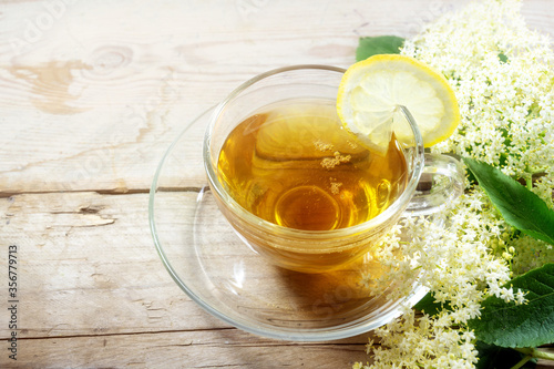 Elderflower tea with lemon and some blossoms on a rustic wooden table, natural home remedy for blood cleansing and against cold and fever, copy space