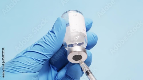 Hand holding glass vial with medical drug being aspirated to a syringe as a treatment or vaccine