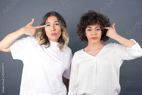 Fotografía Unhappy blonde  woman curves lips and makes suicide gesture, tired of everything, shoots in temple with hand, isolated against studio background