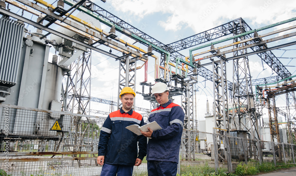 Two specialist electrical substation engineers inspect modern high-voltage equipment. Energy. Industry Two specialist electrical substation engineers inspect modern high-voltage equipment. Energy. Industry