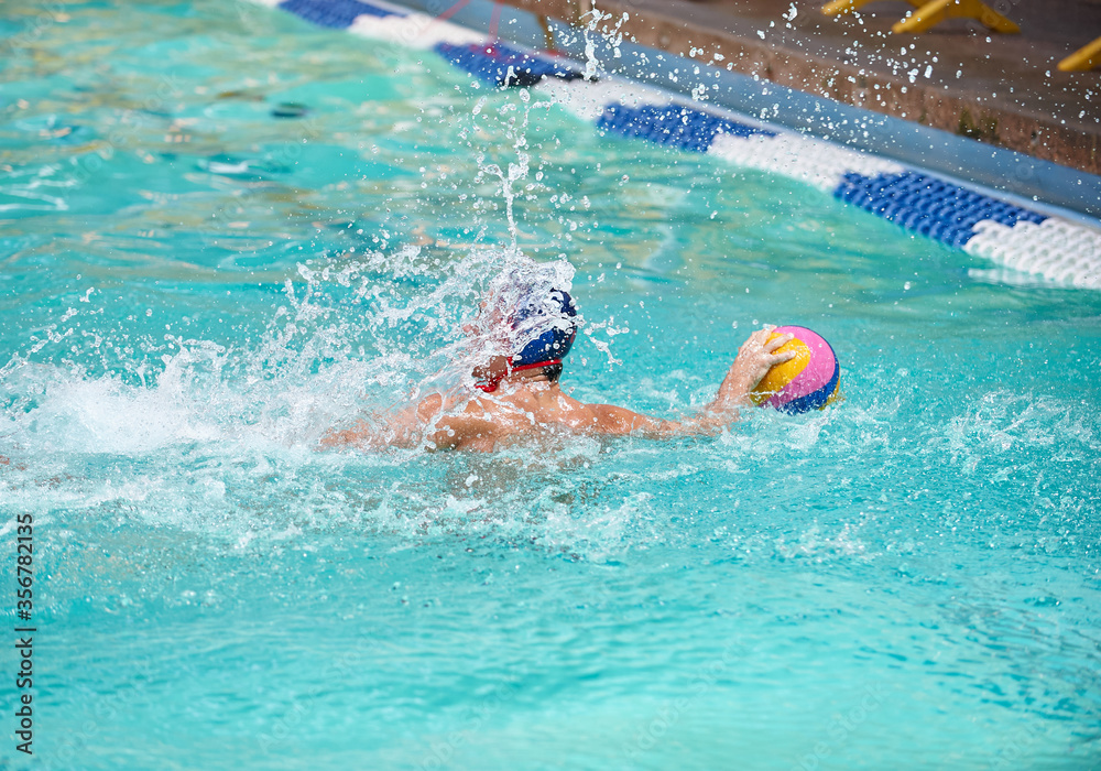 Water polo player in a swimming pool getting splashed with water holding a ball