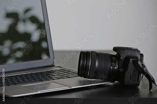 A generic professional digital reflex camera with its big lens leaning on a laptop. A concept about photography bussiness. In the reflective screen, some spots are visible. Plenty of negative space.