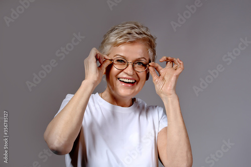 Beautiful blonde mature woman with pixie hair cut having fun and holding glasses photo