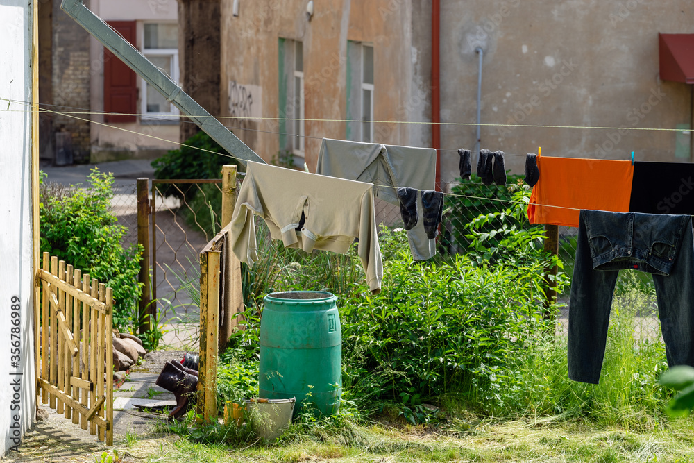 Naklejka premium Clean different laundry are dried outside in the yard on a clothing line in the city. Black shoes are ventilated at the gates. On blurred old houses background. Concept of cleanliness and cleansing