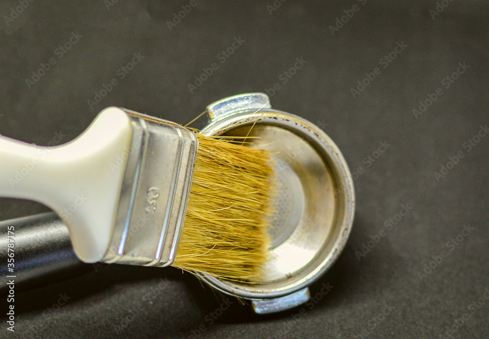 A brush is cleaning espresso machine porta filter.