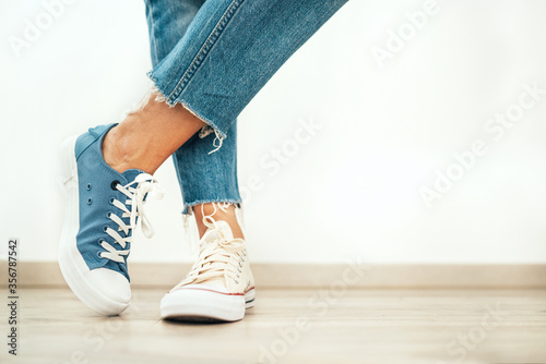 Teenager's feet posing in casual different colors beige and blue new sneakers on the white wooden floor close up image. Vintage style in modern fashion world concept image.