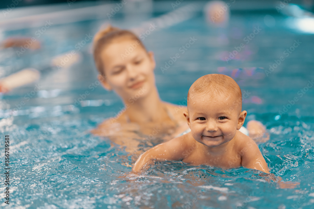 Young mother and her baby enjoying a baby swimming lesson in the pool. Child having fun in water with mom