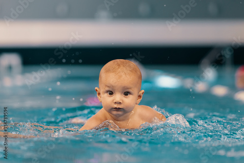 Young mother and her baby enjoying a baby swimming lesson in the pool. Child having fun in water with mom