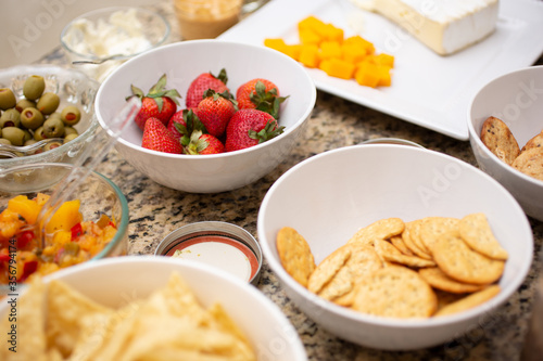 A view of several varieties of party snacks on a marble counter, featuring strawberries, crackers, and cheese bites.