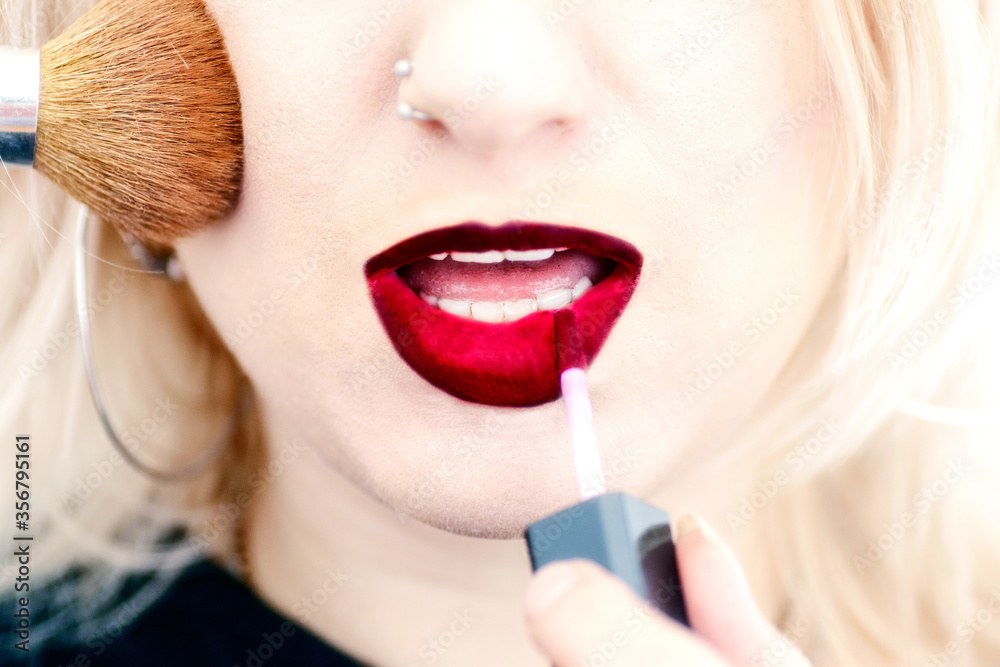 Woman with piercing applying lipstick and powder Woman with piercing applying lipstick and powder