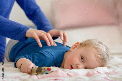 The baby calmly lies on the bed and he is massaged on his back. The girl's hands are visible in the frame.