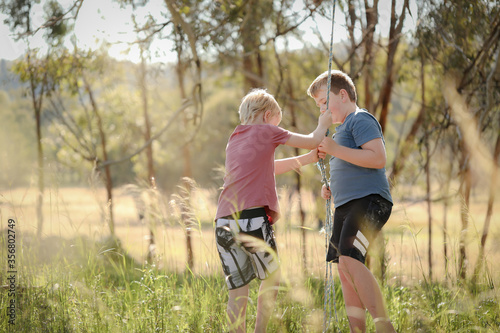 Two brothers playing on rope swing in beautiful bush location. Outdoor play during times of self isolation using imagination.