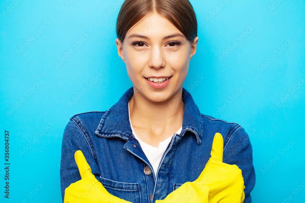 An employee of a cleaning company in overalls and yellow gloves posing on a blue background An employee of a cleaning company in overalls and yellow gloves posing on a blue background