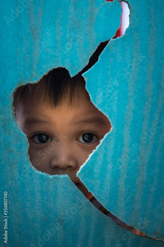 portrait of little boy hiding behind blue cracked plastic wall 