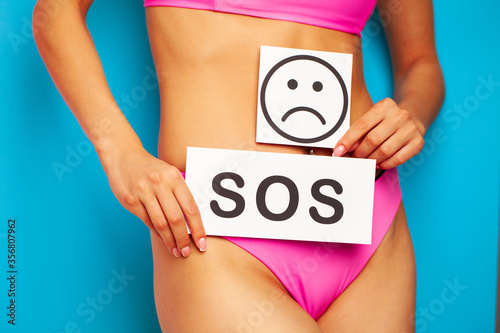 Woman health problem and menstruation pain, closeup of woman's hands holding a sad smile card near her belly