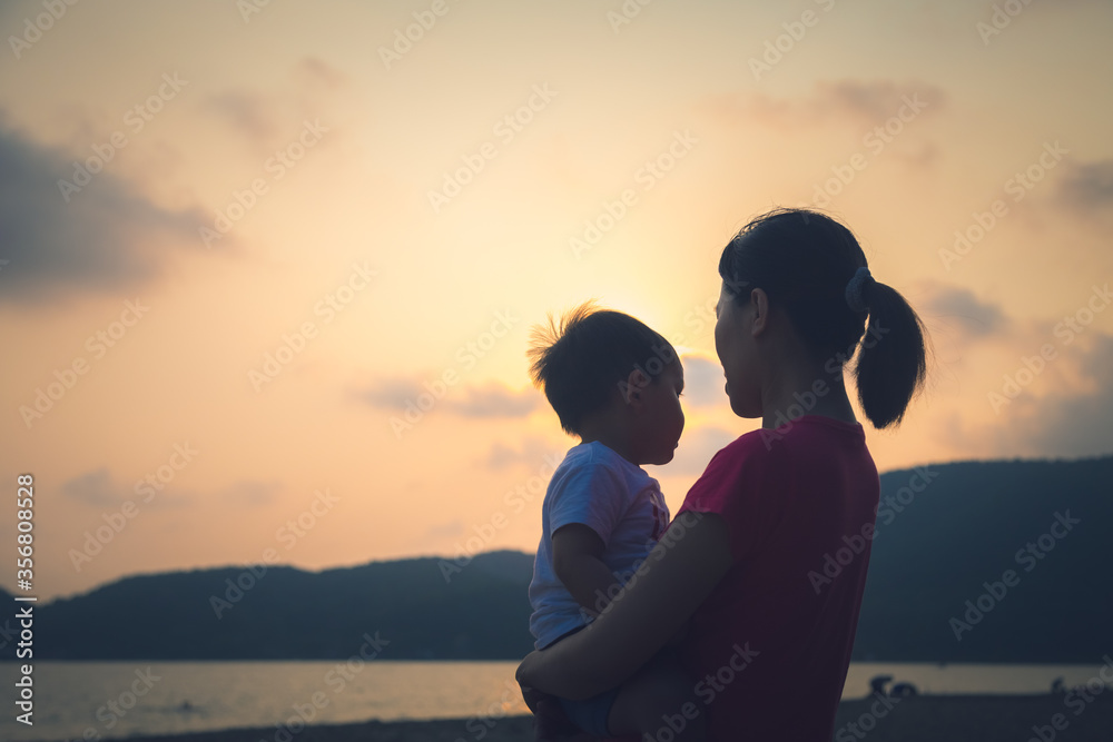 silhouette of Mother holding little child standing  on the beach at sunset 