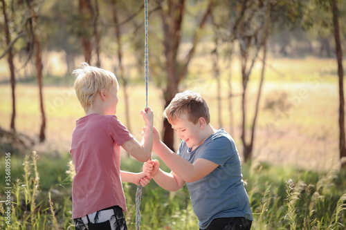 Two brothers playing on rope swing in beautiful bush location. Outdoor play during times of self isolation using imagination.