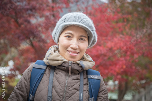 portrait of a young pretty asian woman wearing winter hat and jacket looking and smiling to camera while traveling in autumn season