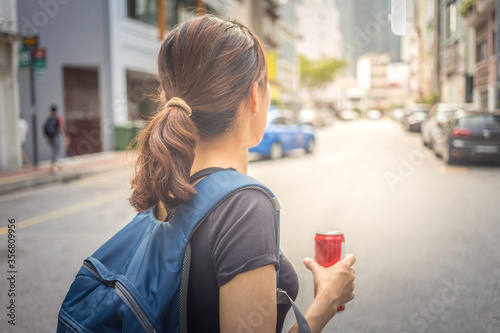 young attractive woman walking on the street holding a can of drinks 