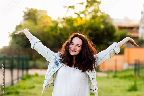 Beautiful young woman arms outstretched and smiles in nature