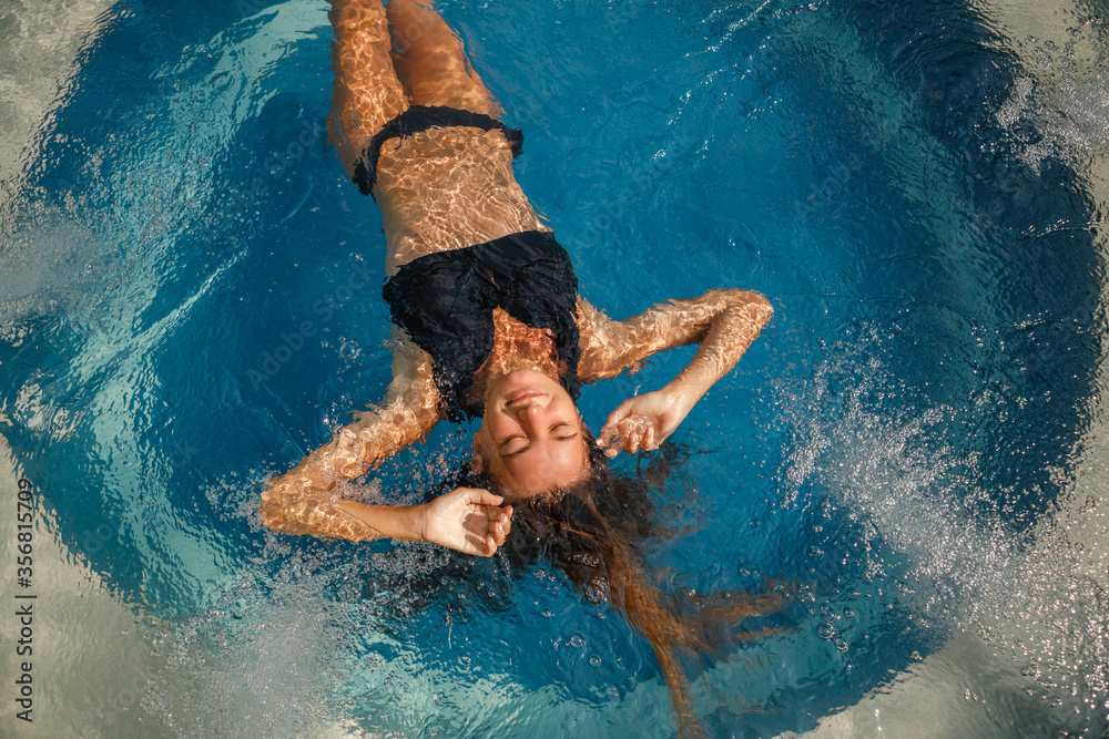 Young woman relaxing in jacuzzi spa in luxury hotel, lie on the back in the water. Woman relaxing in pool with deep blue water in tropical Bali garden - obrazy, fototapety, plakaty 