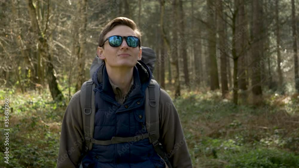 A young hiker walks along a woodland path wearing sunglasses A young hiker walks along a woodland path wearing sunglasses