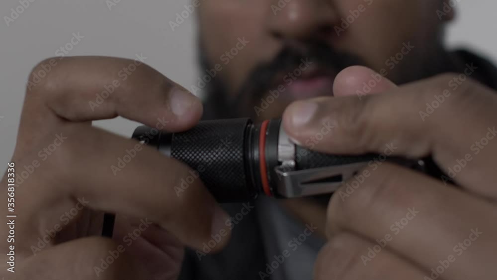 Close Up Of Hands Unscrewing On Battery Cap On Portable LED Torch To Reveal Battery. Low Angle Close Up Of Hands Unscrewing On Battery Cap On Portable LED Torch To Reveal Battery. Low Angle