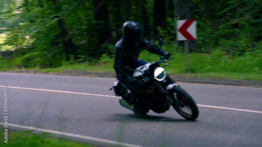 A Motorcyclist leans into the curve on a wide winding asphalt road inside thick forest - Slow Motion panning shot A Motorcyclist leans into the curve on a wide winding asphalt road inside thick forest - Slow Motion panning shot