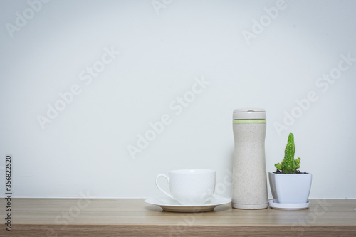 Coffee cup and thermos bottle on table.