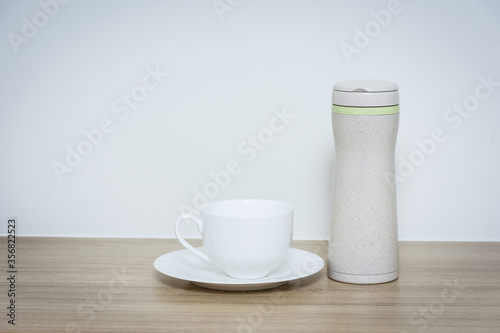 Coffee cup and thermos bottle on table.