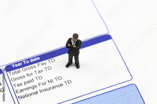 Quadro su tela Miniature scale model businessman standing on a wage pay slip showing earnings deductions