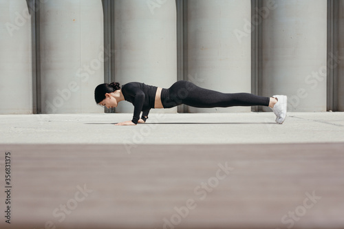 Fitness trainer doing morning push-up exercises on the street in park on the promenade against the background of concrete pipes.