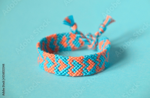 Selective focus of woven friendship bracelet, handmade of thread and knots, with blue, pink hearts pattern. On blue background